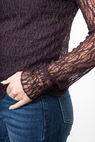 Woman wearing a long sleeve dark purple textured lace top and blue denim jeans.