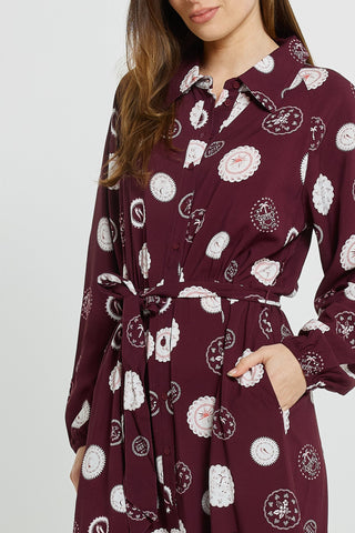Woman wearing a burgundy long-sleeve shirt dress with white circular motifs and a tie waist.