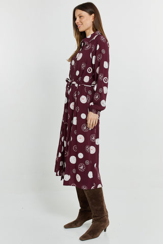 Woman wearing a burgundy midi dress with a white circular print and brown suede boots.