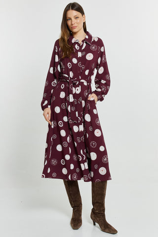 Woman wearing a long-sleeved maroon midi dress with white circular patterns and brown boots