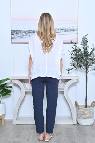Woman wearing a white linen short sleeve blouse and navy blue trousers standing in a bright room.