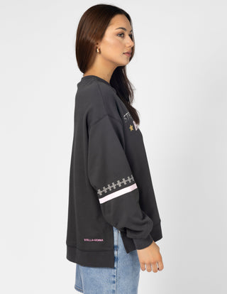 Woman wearing a dark grey long sleeve graphic sweatshirt and light wash denim jeans.