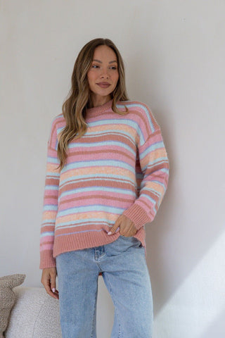 Woman wearing a pastel striped fuzzy sweater and light blue jeans.