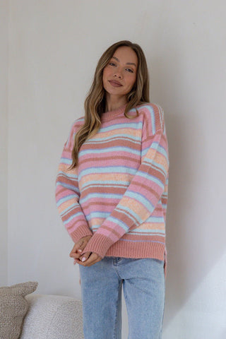 Woman wearing a pastel striped knit sweatshirt and light blue denim jeans.