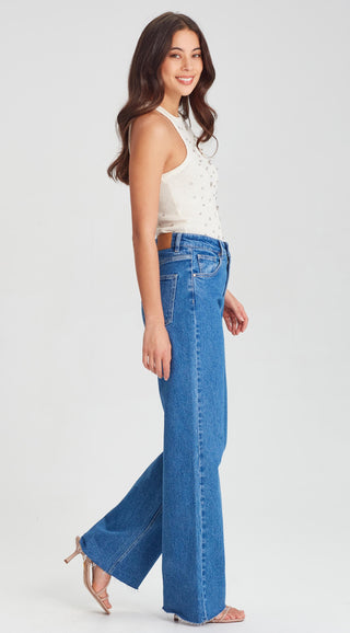 Woman wearing a white embellished top and wide-leg blue jeans with nude heels.