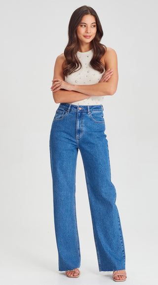 Woman wearing a white beaded sleeveless top and high-waisted wide leg blue jeans.