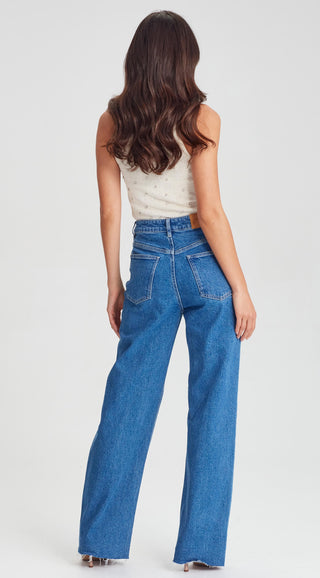 Rear view of a woman wearing a white embellished top and wide-leg blue jeans.