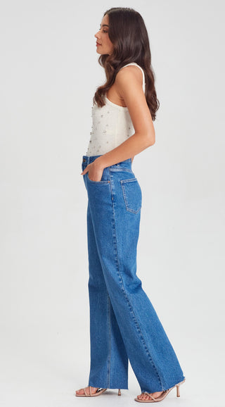 Woman in a white embellished tank top and wide leg blue jeans with beige heels
