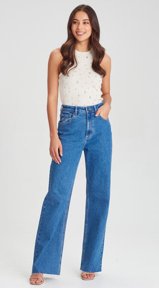 Woman wearing a white pearl-embellished sleeveless top and blue wide-leg jeans.