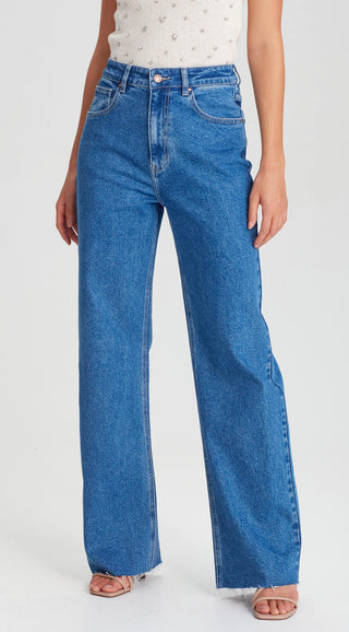 Woman wearing high-waisted wide-leg blue denim jeans and a white beaded top.