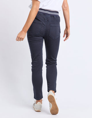 Rear view of a woman wearing dark navy slim-fit trousers and white sneakers.
