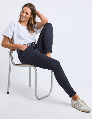 Woman wearing a white t-shirt and navy blue leisure pants sitting on a chair.