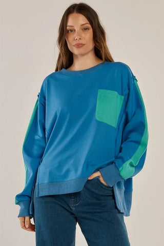 Woman wearing a blue oversized sweatshirt with green accents and blue jeans.