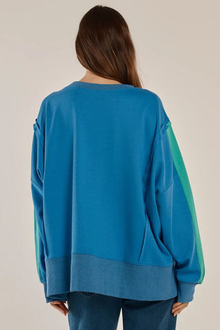 Back view of a woman wearing an oversized blue sweatshirt with green sleeve accents.