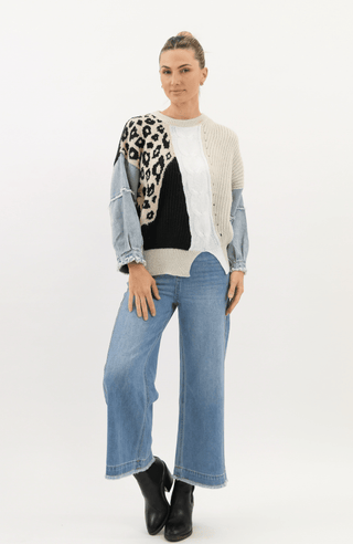 Woman wearing a multi-patterned patchwork knit sweater and wide-leg blue jeans.