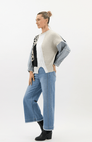 Woman wearing a multi-colored patchwork knit sweater and wide-leg denim jeans.