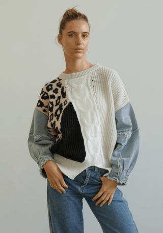 Woman wearing a multi-patterned patchwork knit sweater with leopard print and denim sleeves.
