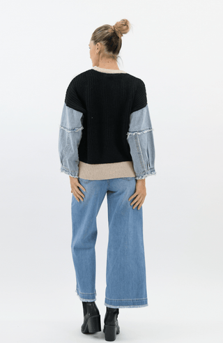 Woman wearing a black and denim mixed-media sweatshirt with wide-leg blue jeans.