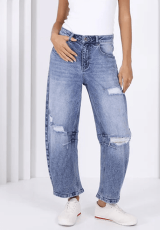 Woman wearing blue distressed wide leg denim jeans and white sneakers.