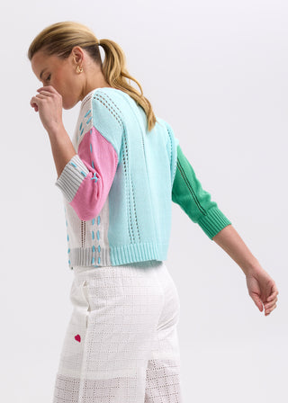 Woman wearing a colorful pastel knit cardigan and white eyelet lace trousers.