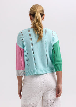 Rear view of a woman wearing a multi-colored knitted cardigan and white eyelet pants.