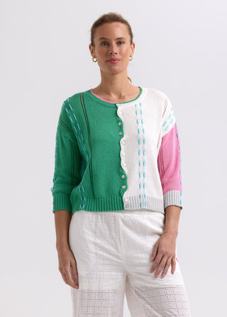 Woman wearing a colorful green, white, and pink color-block knit cardigan with white eyelet pants.