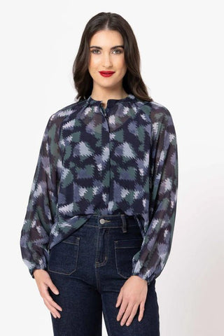 Woman wearing a navy and teal patterned long sleeve blouse with dark denim jeans.