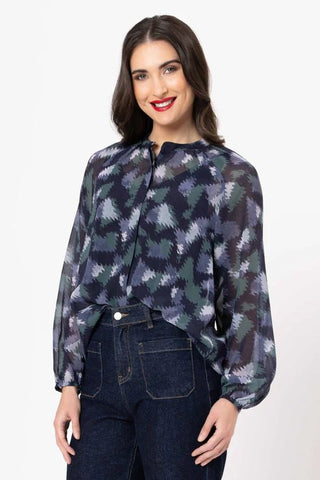 Woman wearing a navy blue patterned long sleeve blouse and dark denim jeans.