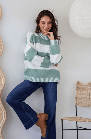 Woman wearing a green and white striped knit sweater and dark blue flare jeans.
