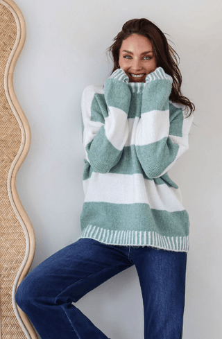 Woman wearing a sage green and white striped oversized knit sweater and blue jeans.
