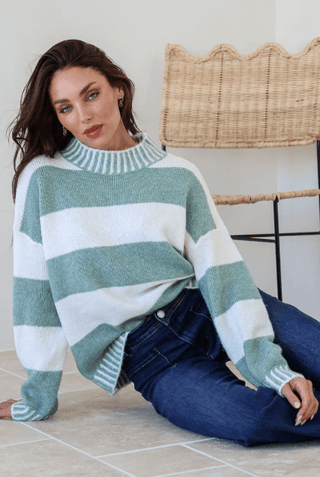 Woman wearing a sage green and white striped knit sweater and blue jeans.