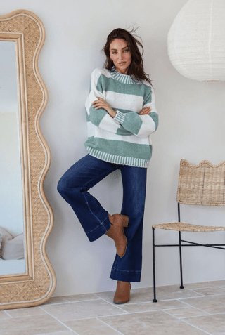 Woman wearing a green and white striped sweater with dark blue wide-leg jeans and brown boots.