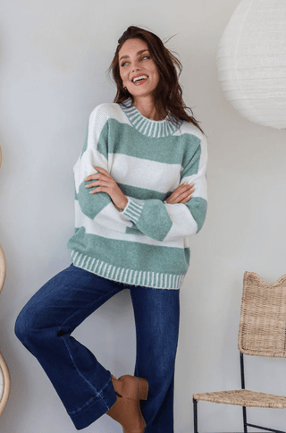 Woman wearing a green and white striped sweater and navy blue flare jeans.