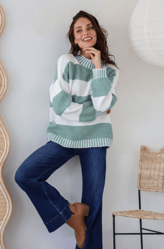 Woman wearing a white and sage green striped oversized knit sweater and dark blue flare jeans
