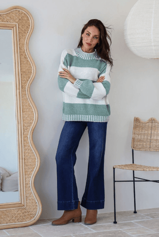 Woman wearing a white and green striped sweater with flared blue jeans and brown boots.