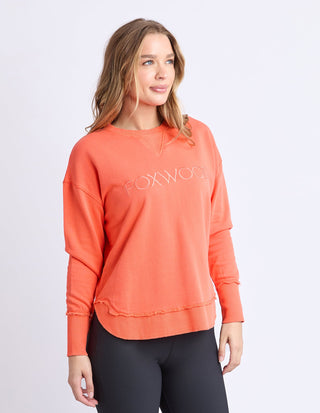 Woman wearing an orange Foxwood sweatshirt with raw edge hem and black leggings