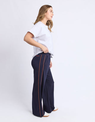 Woman wearing navy wide-leg lounge pants with orange side stripes and a white t-shirt.