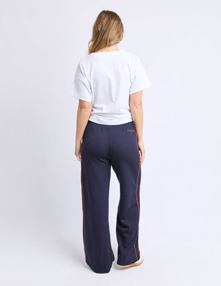 Woman wearing navy blue wide-leg leisure pants with orange side stripe detailing.