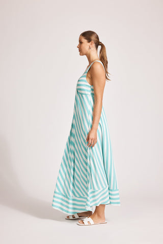 Woman wearing a teal and white striped maxi dress and white sandals.