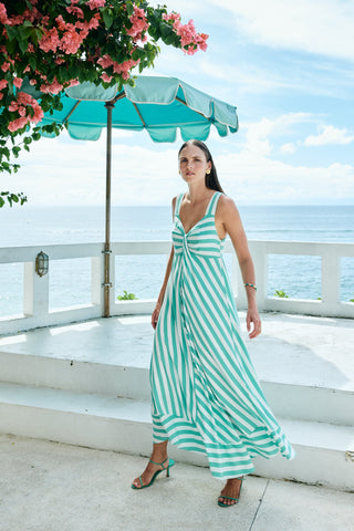 Woman wearing a teal and white striped maxi dress on a sunny seaside terrace.