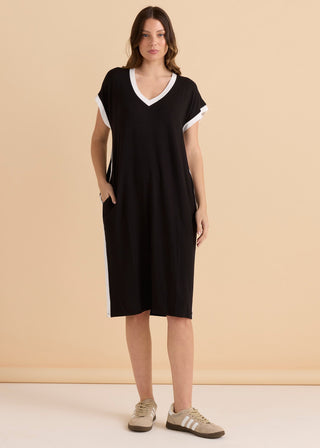 Woman wearing a black v-neck midi dress with white trim and side pockets.