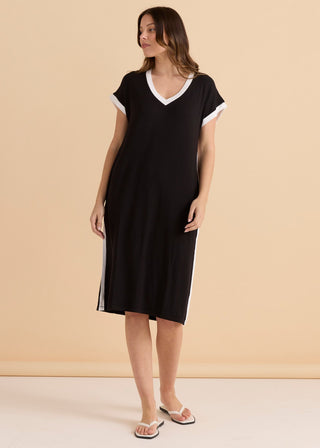 Woman wearing a black midi t-shirt dress with white V-neck and side stripe details.