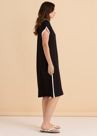 Woman wearing a black midi dress with white trim accents and white flip flops.
