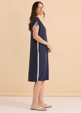 Woman wearing a navy blue sleeveless midi dress with white side stripe detailing.