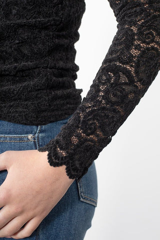 Close-up of a woman wearing a black lace long-sleeve top and blue denim jeans.