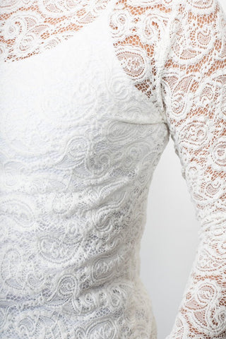 Close-up of a white lace long sleeve dress with intricate floral patterns.