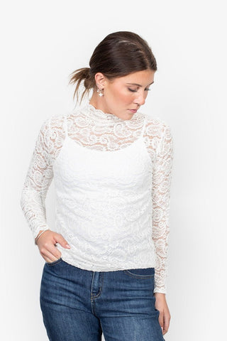 Woman wearing a white long sleeve lace mock neck top and blue denim jeans.
