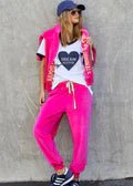 Woman wearing bright pink joggers, a white graphic t-shirt, and a matching pink vest.