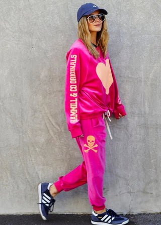 Woman in pink velvet sweatshirt with heart and matching joggers with skull graphic.