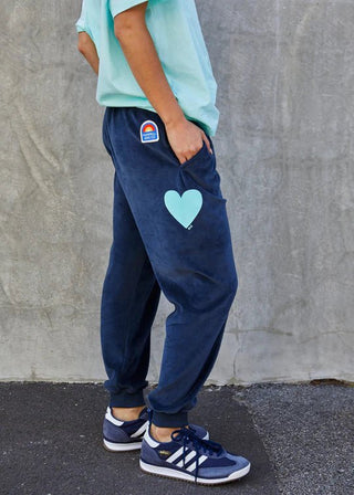Woman wearing navy blue velvet joggers with a light blue heart graphic and casual sneakers.